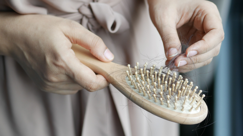 Close-up of a person's hands removing a clump of fallen hair from a wooden-handled hairbrush.